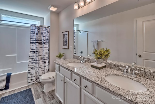 bathroom with toilet, a sink, double vanity, and wood finished floors