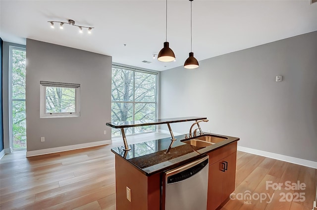 kitchen with dark countertops, light wood-style floors, a healthy amount of sunlight, stainless steel dishwasher, and a sink