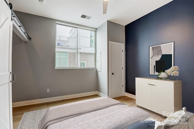 bedroom with visible vents, baseboards, light wood-type flooring, and a barn door