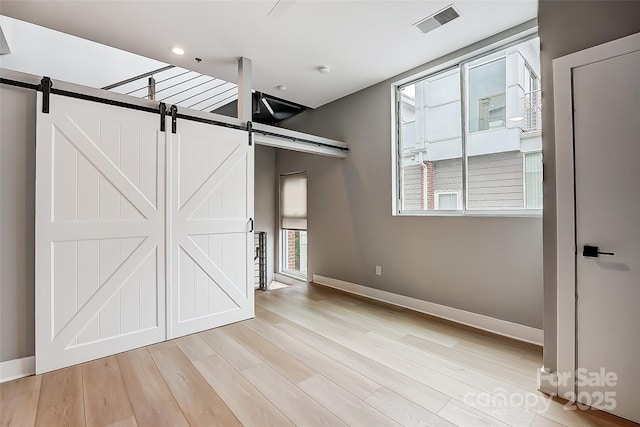 interior space with visible vents, baseboards, a barn door, and light wood-style floors