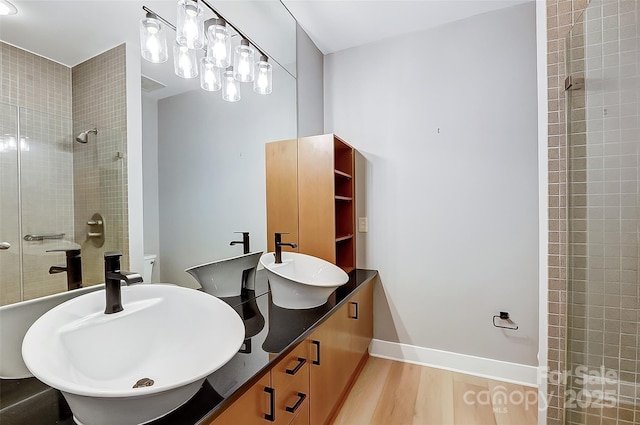 full bathroom featuring a tile shower, baseboards, a sink, and wood finished floors