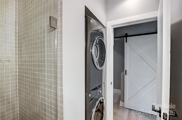 washroom featuring laundry area, a barn door, and stacked washer / drying machine