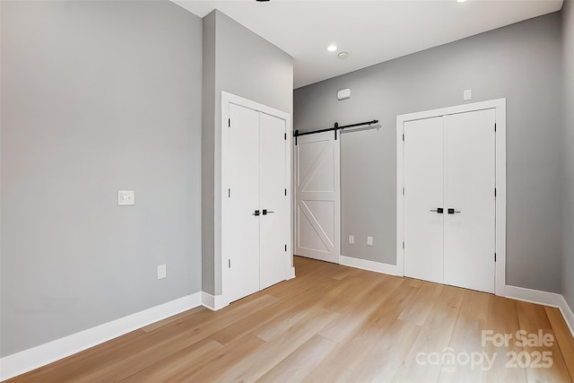 unfurnished bedroom with baseboards, recessed lighting, a barn door, multiple closets, and wood finished floors