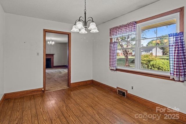 spare room with a fireplace, visible vents, a chandelier, wood finished floors, and baseboards