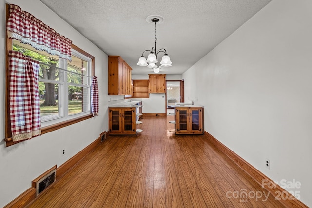 unfurnished dining area with visible vents, baseboards, a chandelier, a textured ceiling, and wood-type flooring