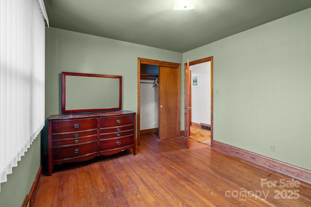 bedroom featuring baseboards, wood finished floors, a closet, and visible vents