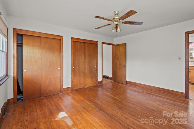 unfurnished bedroom with visible vents, baseboards, multiple closets, and wood finished floors