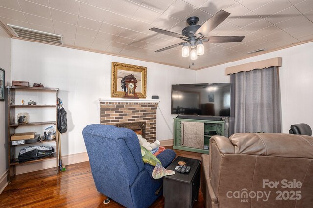 living room with visible vents, ceiling fan, a brick fireplace, and wood finished floors