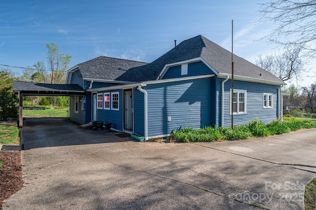 view of side of property with roof with shingles, concrete driveway, and an attached carport