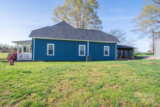 rear view of property with a shingled roof, cooling unit, and a lawn