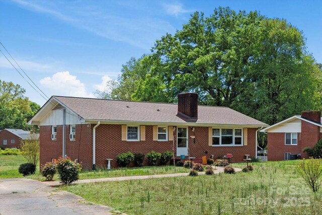 ranch-style home with brick siding, a chimney, central air condition unit, and a front lawn