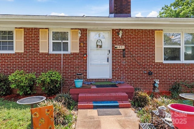 view of exterior entry with brick siding and a chimney