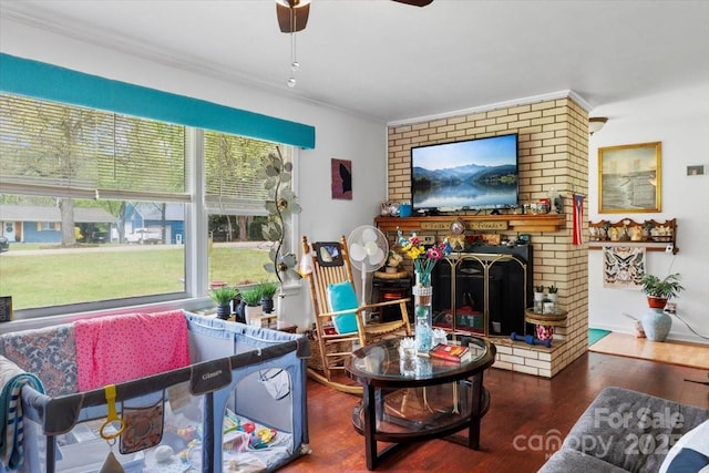 living area featuring ornamental molding, a ceiling fan, wood finished floors, and a brick fireplace