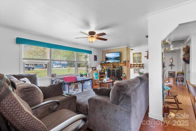 living room featuring ceiling fan, a brick fireplace, ornamental molding, and wood finished floors