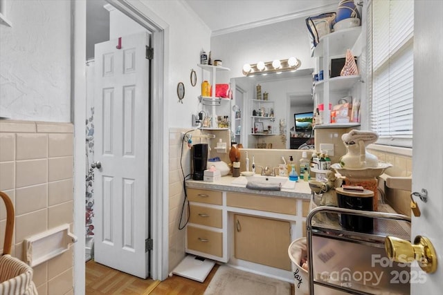 bathroom featuring tile walls, crown molding, wainscoting, and vanity