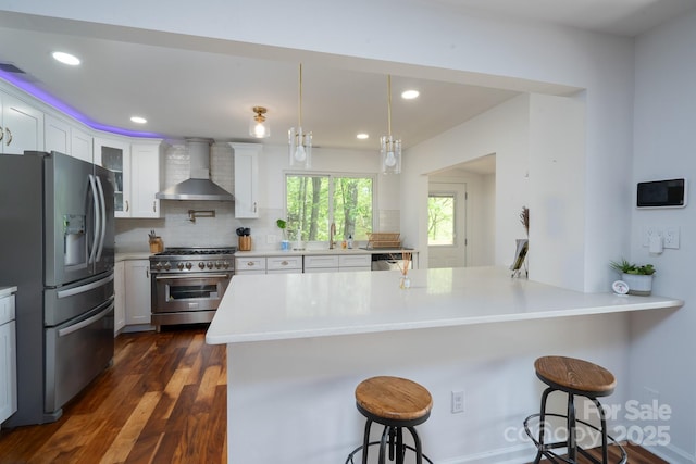 kitchen with wall chimney exhaust hood, a breakfast bar, appliances with stainless steel finishes, light countertops, and backsplash