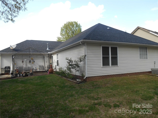 back of property featuring roof with shingles, a patio area, and a lawn