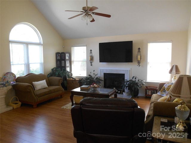 living area featuring ceiling fan, high vaulted ceiling, wood finished floors, and a fireplace