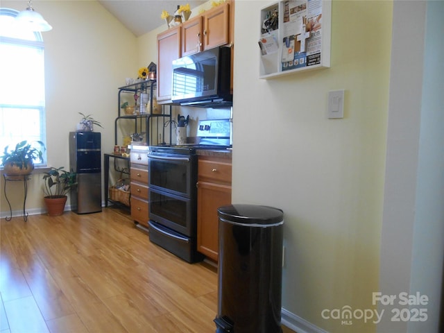 kitchen featuring black microwave, light wood-type flooring, double oven range, dark countertops, and brown cabinets