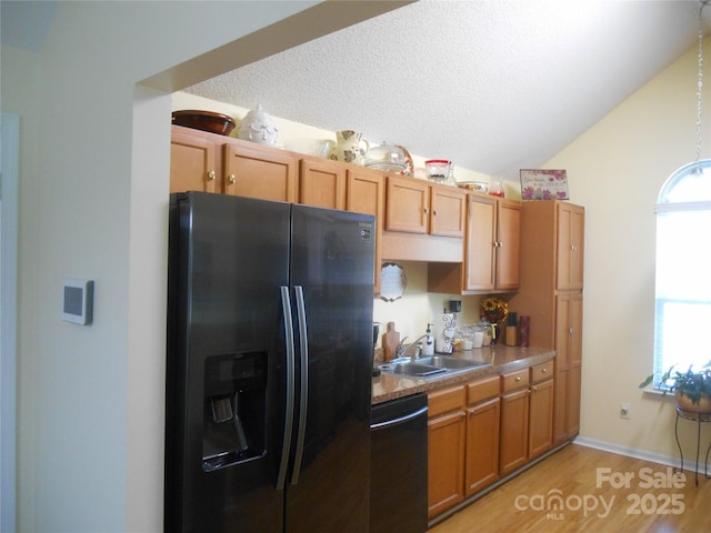 kitchen with dishwashing machine, brown cabinetry, vaulted ceiling, a sink, and black fridge with ice dispenser