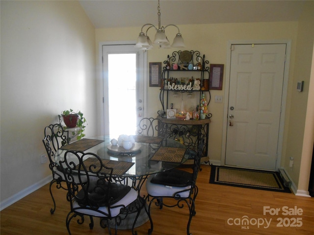 dining area with wood finished floors, an inviting chandelier, baseboards, and lofted ceiling