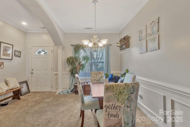 carpeted dining area featuring a notable chandelier, crown molding, visible vents, wainscoting, and arched walkways