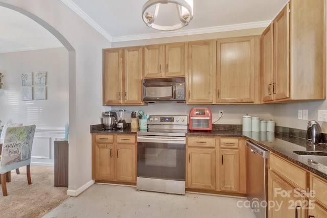 kitchen featuring ornamental molding, dark stone counters, appliances with stainless steel finishes, arched walkways, and a sink