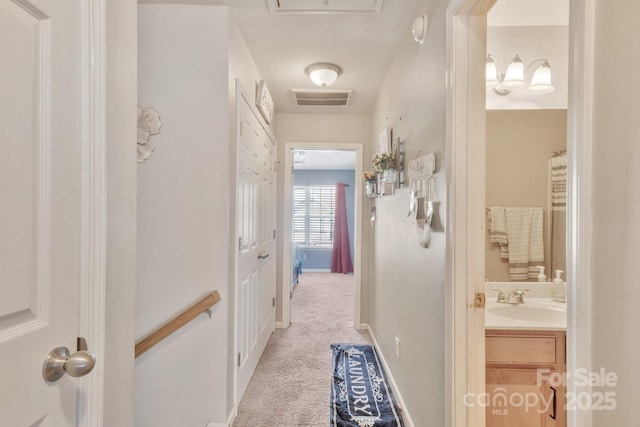 corridor with baseboards, visible vents, light colored carpet, and a sink