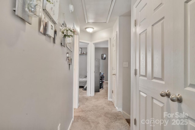 corridor with light carpet, baseboards, and attic access