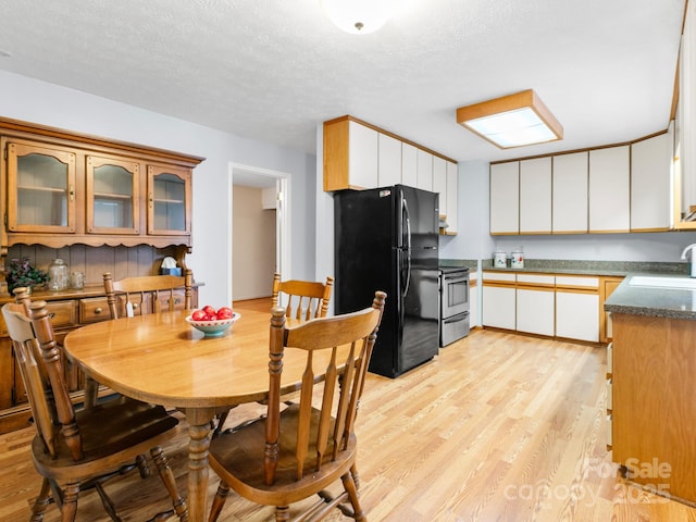 kitchen with a sink, dark countertops, light wood-type flooring, freestanding refrigerator, and stainless steel range with electric cooktop