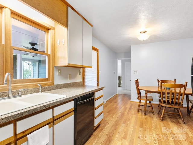 kitchen with white cabinetry, a ceiling fan, light wood finished floors, dishwasher, and a sink