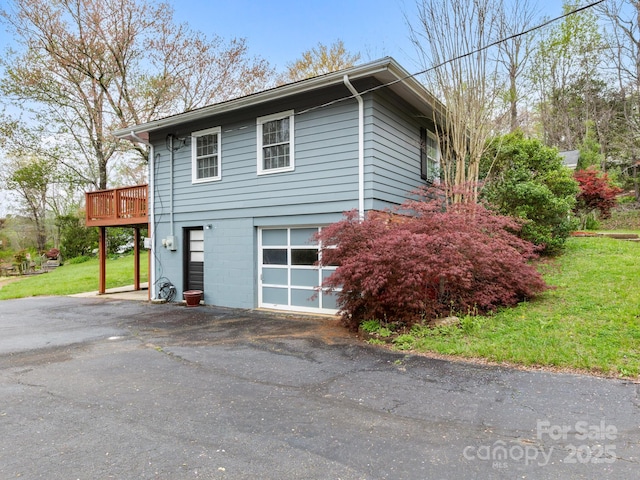 view of property exterior with an attached garage, a yard, driveway, and a wooden deck