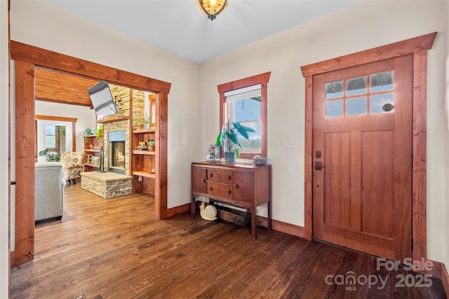 entryway featuring a stone fireplace, baseboards, and wood finished floors
