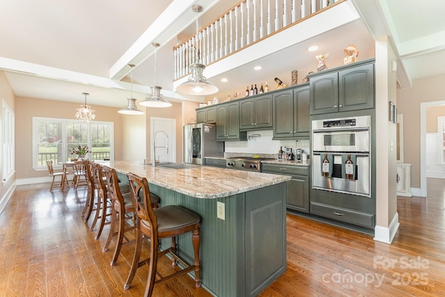 kitchen featuring baseboards, a chandelier, light wood-style flooring, appliances with stainless steel finishes, and a sink
