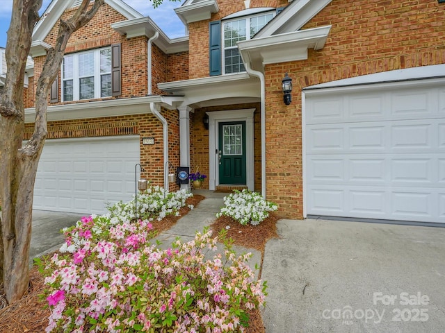 entrance to property featuring brick siding, concrete driveway, and an attached garage