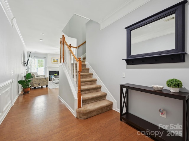 stairway with a fireplace, wood finished floors, crown molding, and baseboards