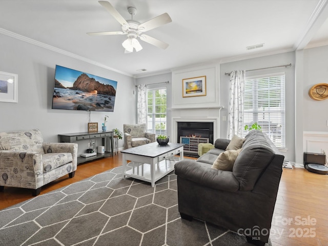 living room featuring crown molding, visible vents, wood finished floors, and a glass covered fireplace