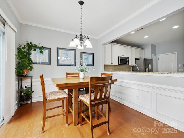 dining room with light wood finished floors, a chandelier, and ornamental molding