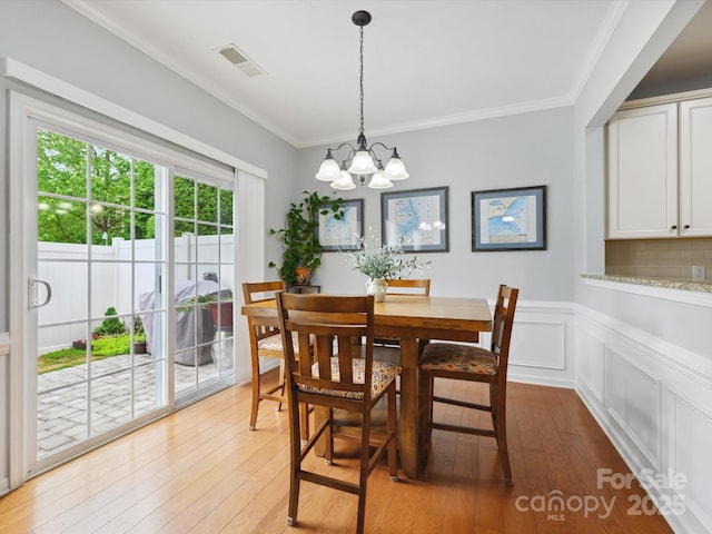dining area featuring visible vents, a chandelier, light wood-type flooring, ornamental molding, and wainscoting