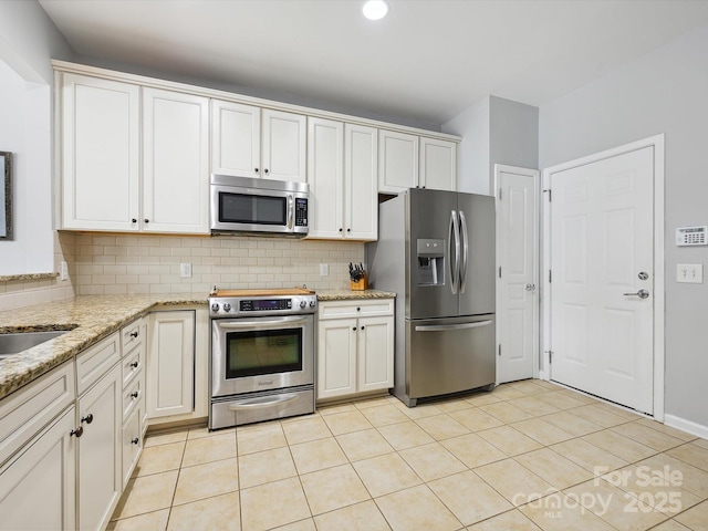 kitchen with light stone countertops, decorative backsplash, stainless steel appliances, white cabinetry, and light tile patterned flooring