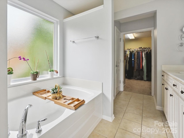 bathroom with vanity, a healthy amount of sunlight, a walk in closet, a garden tub, and tile patterned flooring