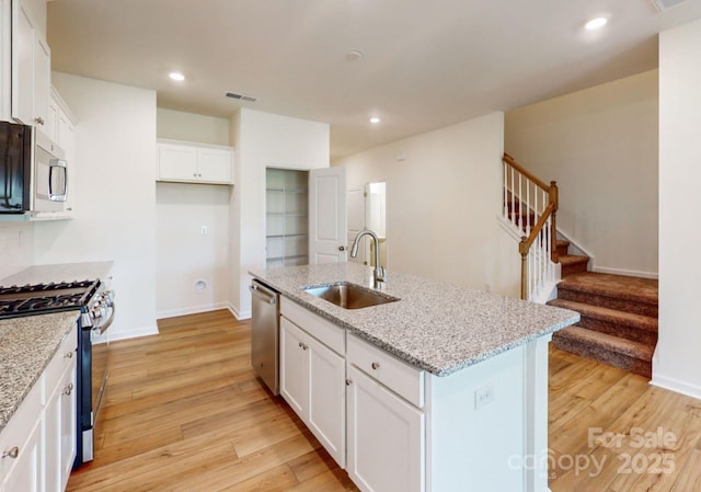 kitchen featuring white cabinetry, a kitchen island with sink, stainless steel appliances, light wood finished floors, and a sink