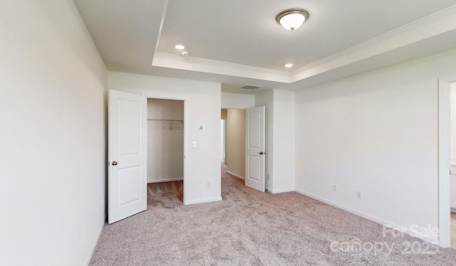 unfurnished bedroom featuring a spacious closet, carpet flooring, crown molding, visible vents, and a tray ceiling