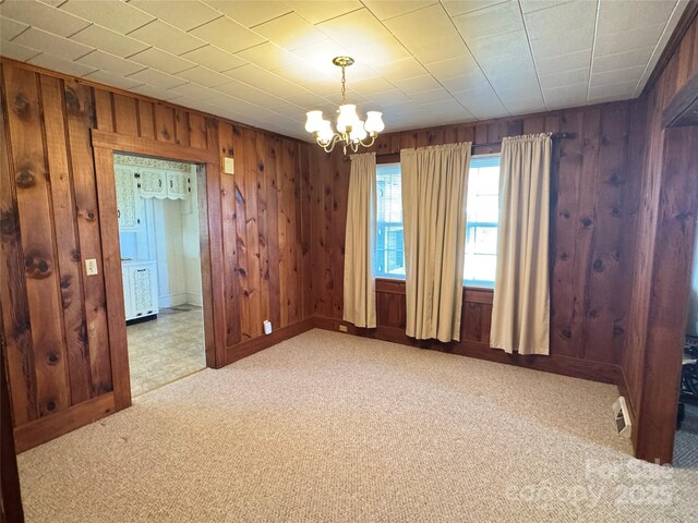 unfurnished room with wood walls, an inviting chandelier, baseboards, and carpet floors