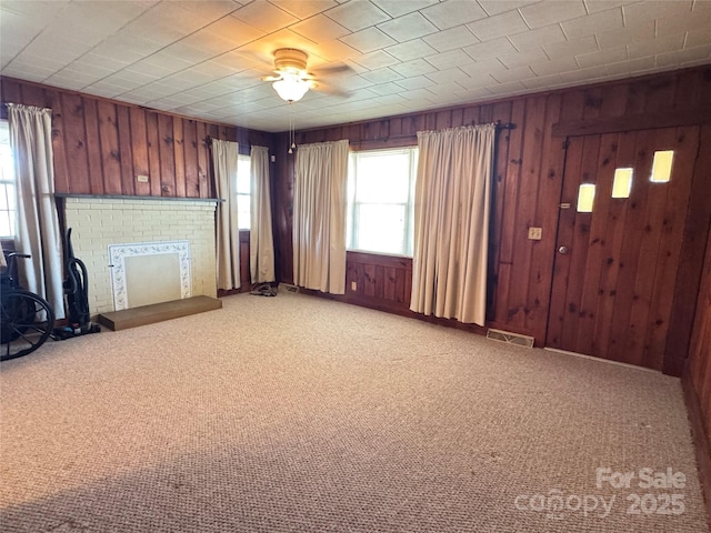 unfurnished living room with wood walls, visible vents, ceiling fan, and light carpet
