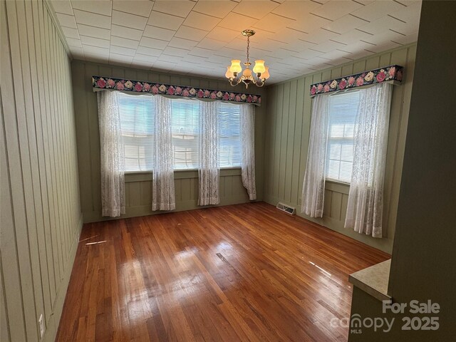 empty room featuring a chandelier, visible vents, wood finished floors, and wood walls