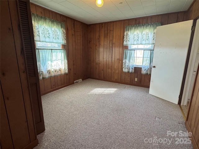spare room featuring carpet flooring, visible vents, and wood walls