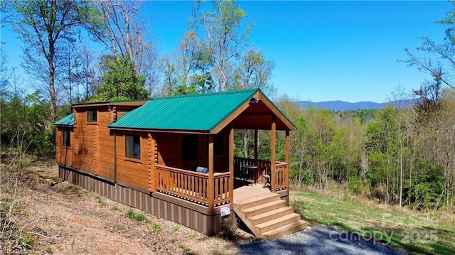 rear view of property featuring metal roof, log exterior, a forest view, and a mountain view