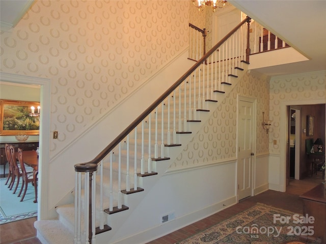 stairway featuring ornamental molding, visible vents, a wainscoted wall, a high ceiling, and wallpapered walls