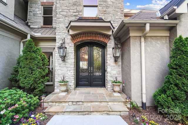 entrance to property featuring french doors, stucco siding, and stone siding